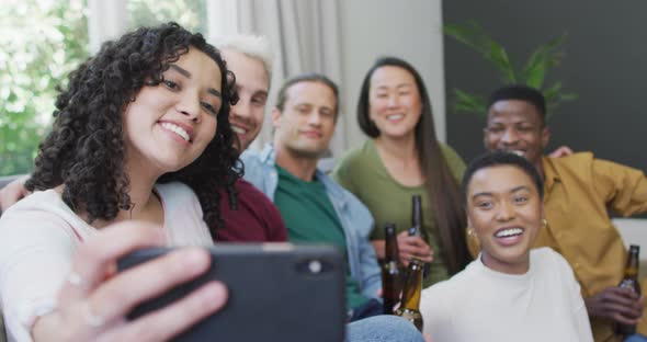 Diverse group of happy male and female friends smiling and taking selfie in living room alt