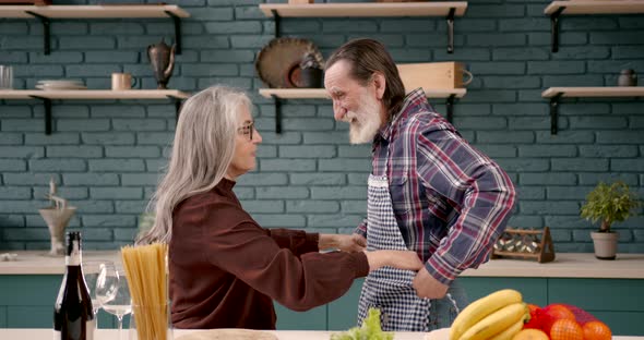 Senior Couple Putting on Aprons Before Preparing Food in Kitchen