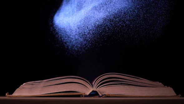 A Beam of Light Illuminates the Pages of an Open Book on a Table in a Dark Studio alt