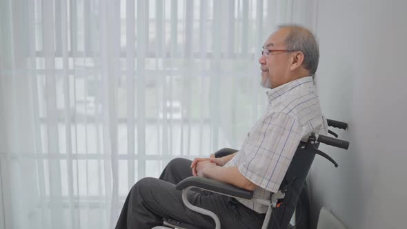 Asian senior man sitting alone on the wheelchair looking out of window