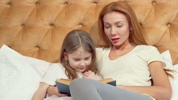 Little Girl and Her Mom Smiling To the Camera Reading a Book alt