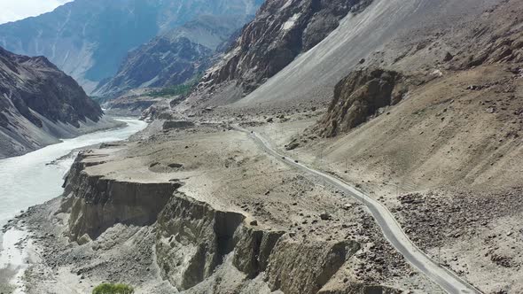 aerial drone overlooking a dirt highway road and large mountain cliff with the Indus River Valley be alt