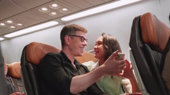 Happy Man and woman in love traveling see smartphone and smile together on the airplane