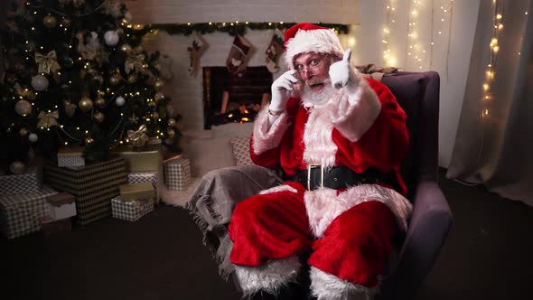 Portrait of a Cheerful Santa Claus in Glasses, Sitting in His Rocking Chair and Showing a Thumbs Up