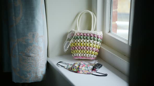 Woman grabbing cute bag and puts items in to leave house, face mask with flower pattern, sunny windo alt