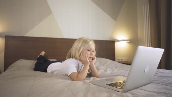 a Cute Preschool Boy Lying on the Bed and Watching a Video on a Laptop. Distance Learning Online