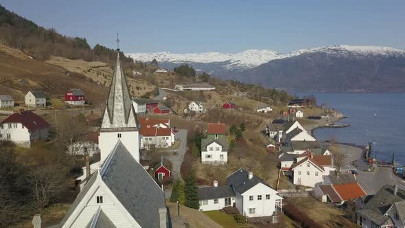 Aerial Shot Orbiting Around a Church Steeple in a Norwegian Village with Snow Capped Mountains and a alt