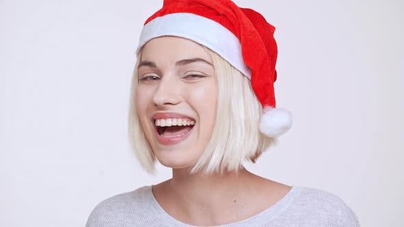 Young Beautiful Blonde Girl in Christmas Hat Smiling Winking Sending Kisses Ovwer White Background alt