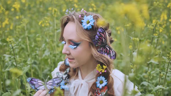 A Young Girl Poses in a Rapeseed Field with a Beautiful Hairdo of Flowers and Butterflies alt