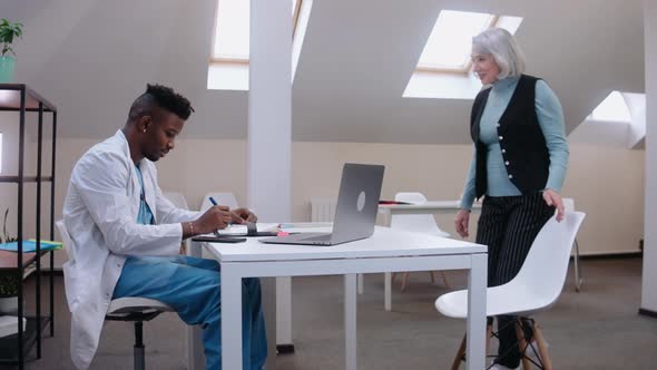 Doctor Sees Elderly Patient Gives Her Consultation Wearing Medical Gown alt