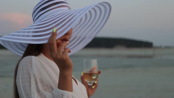 Elegant Woman with Glass of Wine Resting on Beach at Sunset