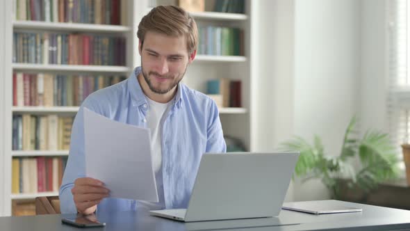 Successful Man Reading Documents While Using Laptop alt