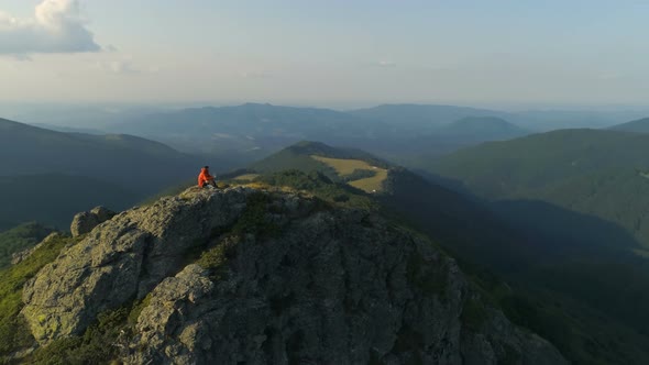 Male Hiker Sitting on Top of Rocky Mountain Peak Looking Down the Deep Valley alt