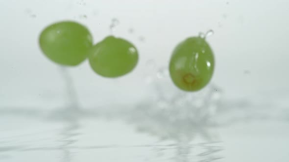 Green grapes falling and bouncing on water surface. Slow Motion. alt