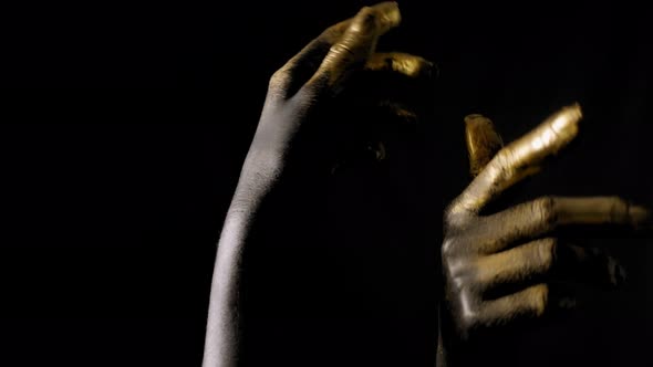 Close-up of a Young Woman's Hands in Black and Gold Paint on Skin in a Dark. alt