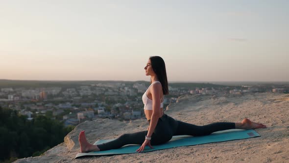 Woman Yoga Sitting in a Twine Pose on Top of Hill at Sunset