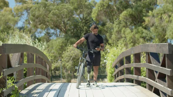 Long Shot of Biker with Disability Taking Selfie in Summer Park alt