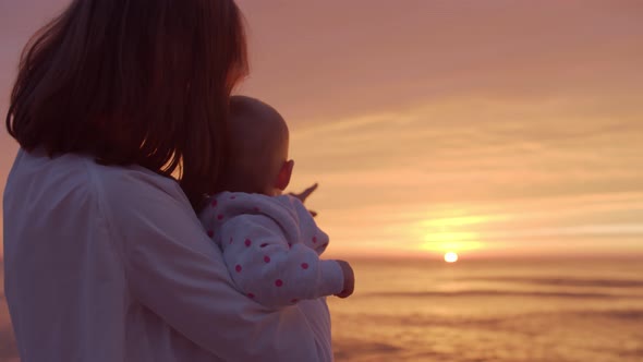 Happy mom hugs her baby at sunset background