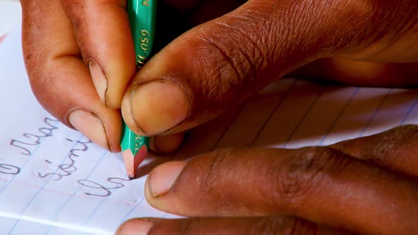 Extreme close up of an African person's hands as they write on lined white paper in a classroom in A alt