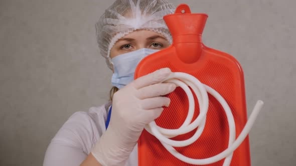 Closeup of a Female Doctor in a Hospital Holding a Hot Water Bottle or Enema alt