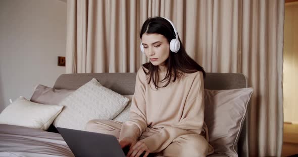 Young Beautiful Woman Using Laptop with Wireless Headphones Sitting in Cozy Bed alt