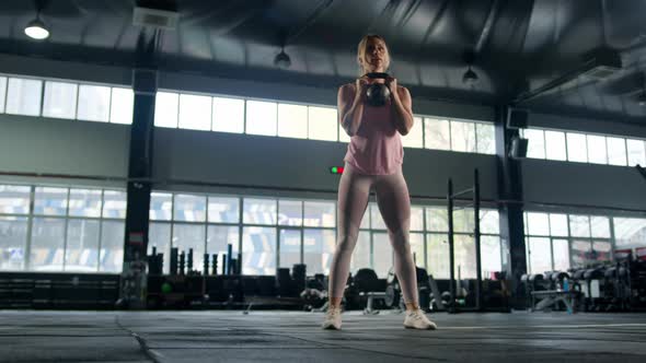 Young female athlete trains with a kettlebell in the gym, squats with a kettlebell, training alt