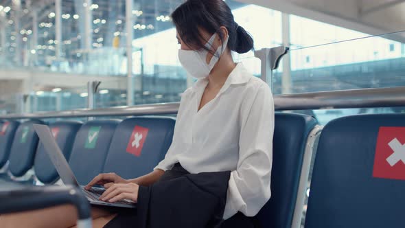 Asian business lady traveller wear face mask sitting in bench use laptop for work between.