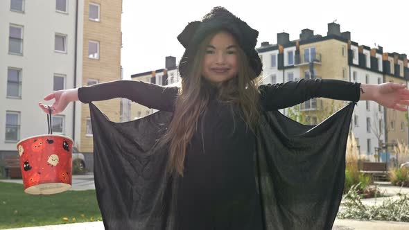 Halloween. A 6-7 Year Old Girl in a Bat Fancy Dress with a Bucket To Collect Sweets. The Child Shows alt