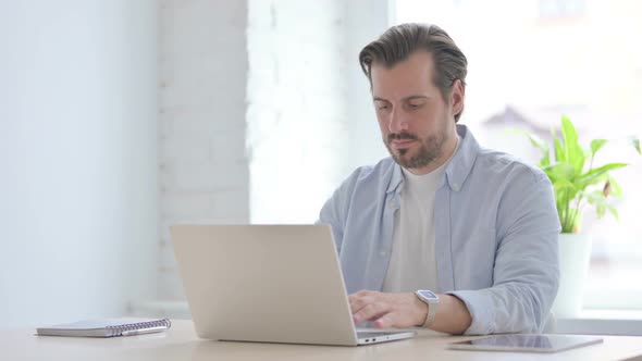 Busy Young Man Typing on Laptop in Office alt