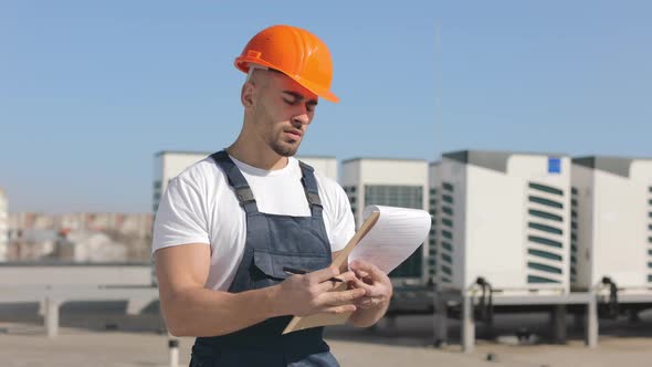 Portrait of a Serious Young Engineer Who is Making Entries in Documents and Looking at the Air alt