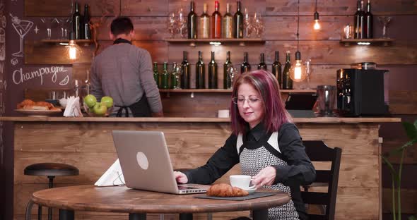 Medium Shot of Adult Businesswoman Typing an Email While Enjoying Her Coffee alt