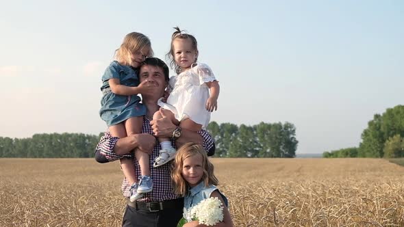 Happy father walks through Golden field of wheat with three daughters alt