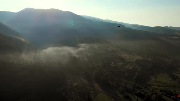 Aerial view of sunrise over foggy village in mountains. alt