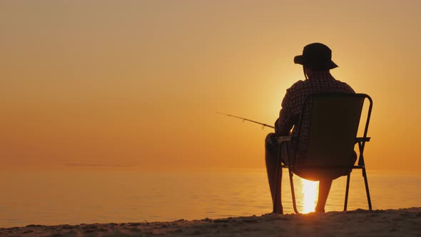 Rear View A Young Man is Sitting on the Seashore Fishing alt