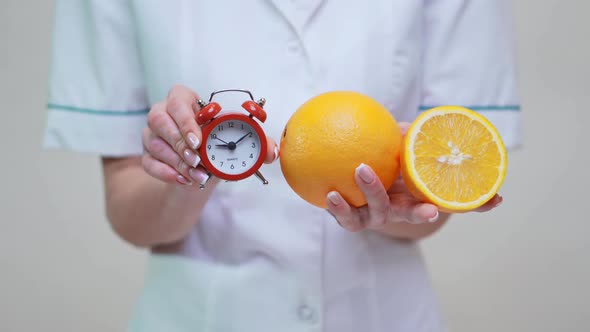 Nutritionist Doctor Healthy Lifestyle Concept - Holding Orange Fruit and Alarm Clock alt