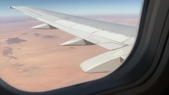 Wide shot of the wing of a large aeroplane in flight shot through the plane window alt
