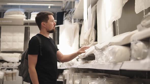 a Young Man Looks at the Sheet He Wants to Put in His Apartment on the Bed alt