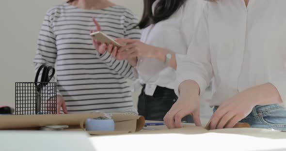 Three Fashion Designer Works at a Table and Discuss About Something Curves and a Pattern Scissors alt