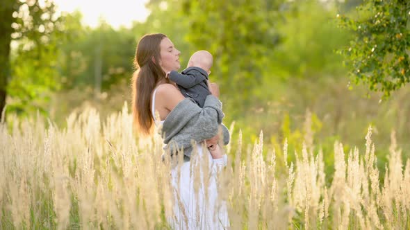 Loving tender mum in a dress with a cute little baby on a field at sunset on a summer
