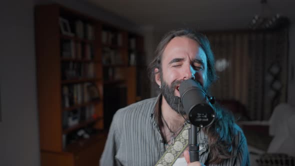 Young Musician Singing and and Playing His Guitar at His Home Studio alt