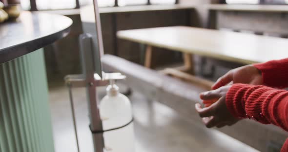 Midsection of african american woman working at a bar, using hand sanitising gel dispenser alt