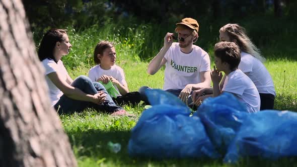 Volunteers Sit on Lawn Family Recycle Plastic Bottle with Bags Full of Trash Resting and Talking alt