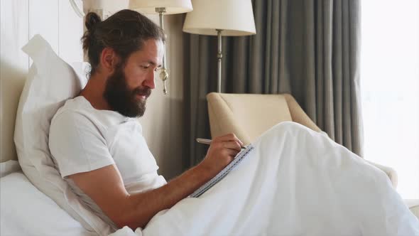Young Bearded Man Writing Notes to Diary After Awake in Bedroom at Home