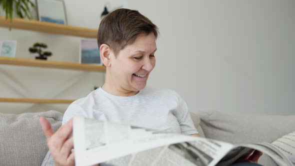 A Closeup View of a Beautiful Mature Woman is Reading a Newspaper Sitting on Sofa at Home in the alt