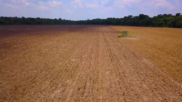 Aerial drone shot following a tractor harvesting a dry field alt