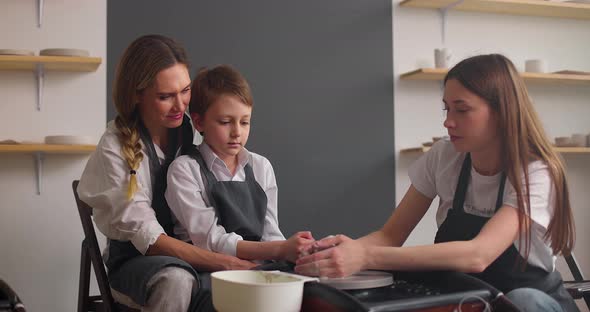 Master Potter Teaching Mother with Her Kid in Pottery Workshop alt