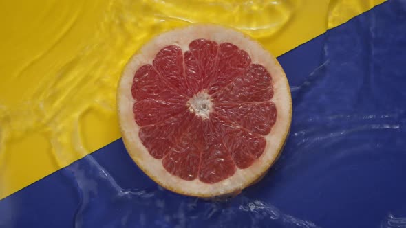 Water Flowing Slow Mo Around Grapefruit Slice on Yellow Blue Backdrop