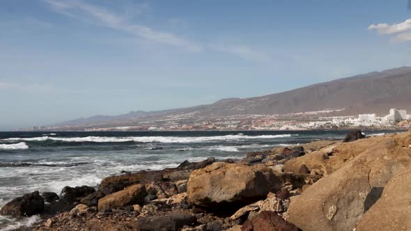 View of the Atlantic waves coming to the rocky shore with a city in the background, Tenerife alt