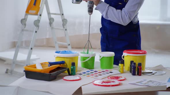 Male Painter Mixes Paint in Bucket with Construction Mixer for Painting Walls Indoors alt