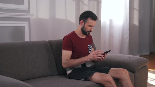 a Man Sits in a Massage Belt on the Couch